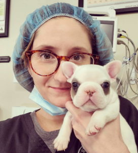 a photo of Tasha McNerney in surgical scrubs holding a tiny puppy.