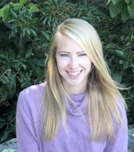 A photo of Charlotte Hacker, PhD, seated outside smiling in a purple top.