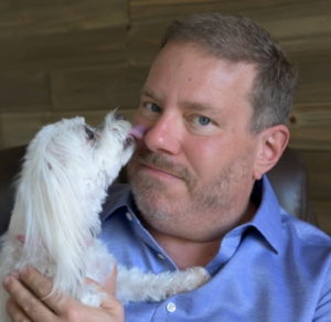 A photo of James Jacobson with his dog Kanga. Kanga is licking his nose.