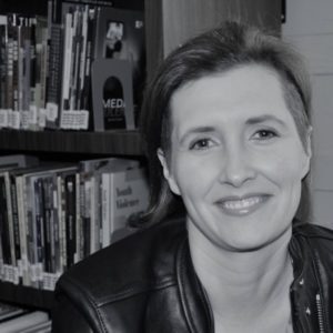 Black and white photo of a woman with her bookcase in the background