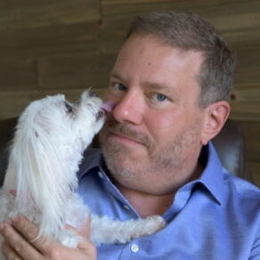 A photo of James Jacobson with his dog Kanga. Kanga is licking his nose.