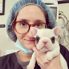 a photo of Tasha McNerney in surgical scrubs holding a tiny puppy.