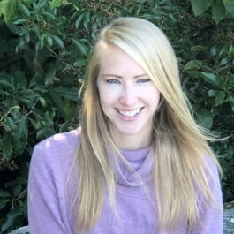 A photo of Charlotte Hacker, PhD, seated outside smiling in a purple top.